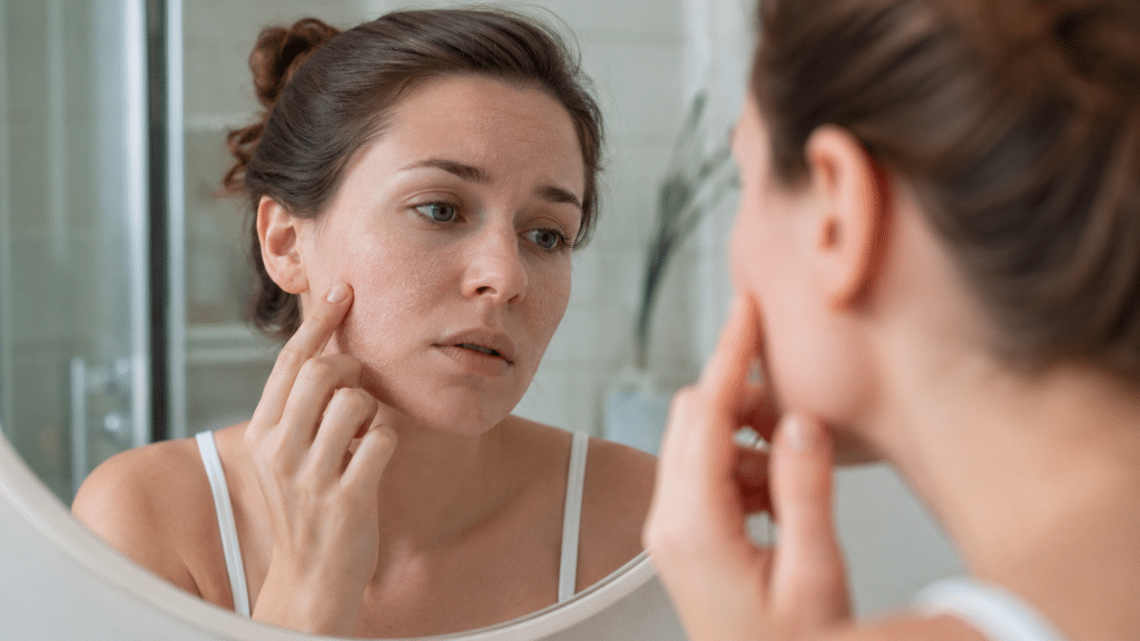 Donna con pelle secca che osserva il viso allo specchio in bagno luminoso