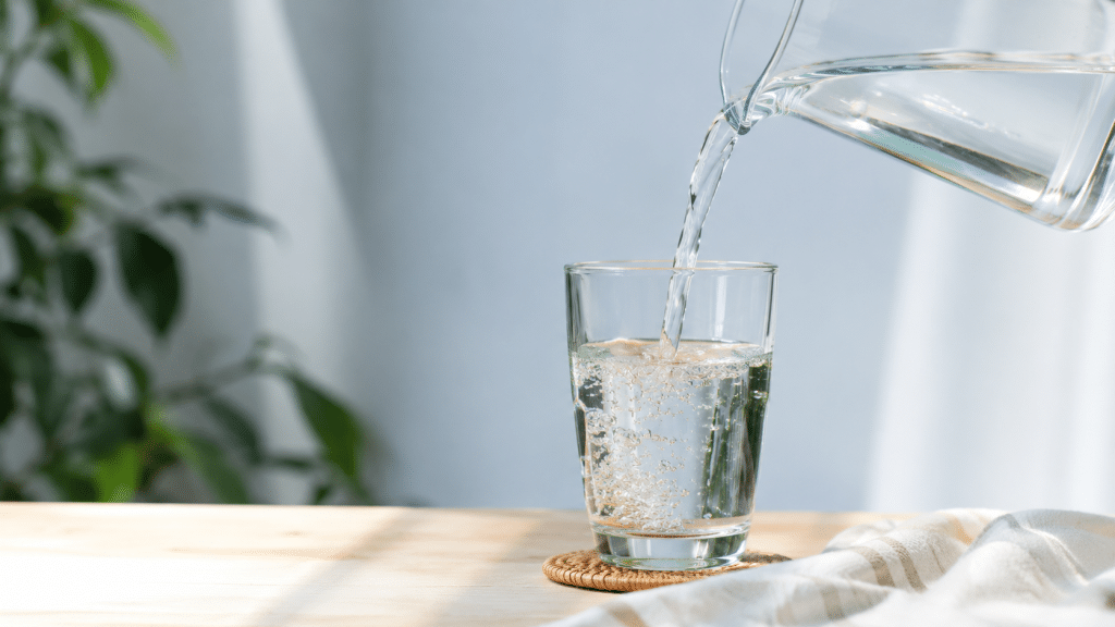 Bicchiere d'acqua fresca su tavolo illuminato dalla luce naturale come simbolo di corretta idratazione.