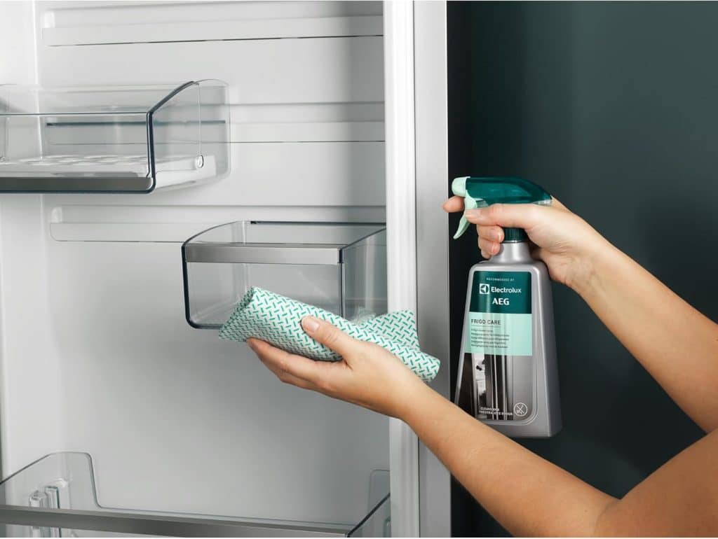 Person cleaning the inside of the refrigerator with a cleaning spray and a microfiber cloth.